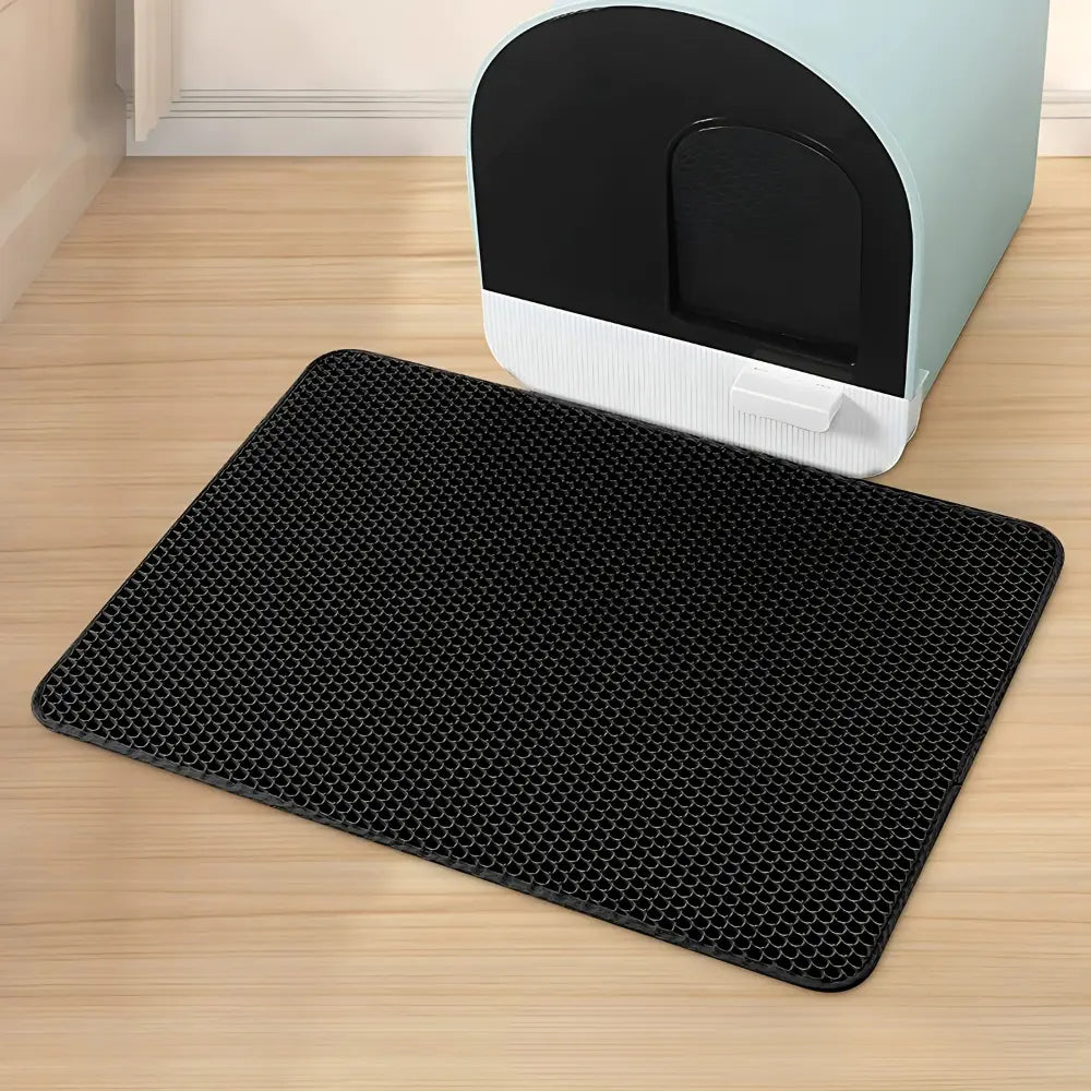 Tapis litière chat PurraMat noir placé devant un bac à litière couvert