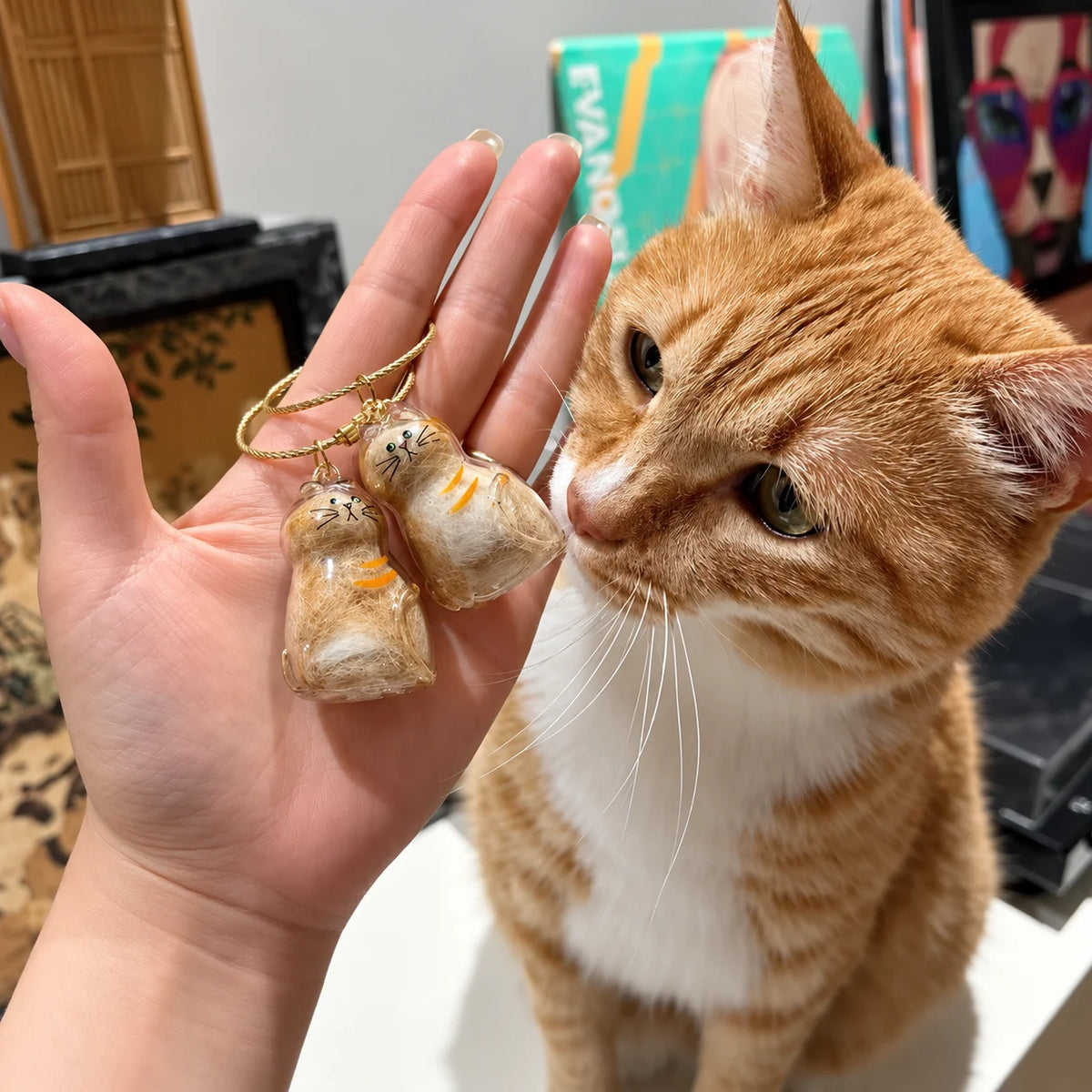 Chat roux curieux près de deux porte-clés commémoratifs PurrKey contenant des poils de chat