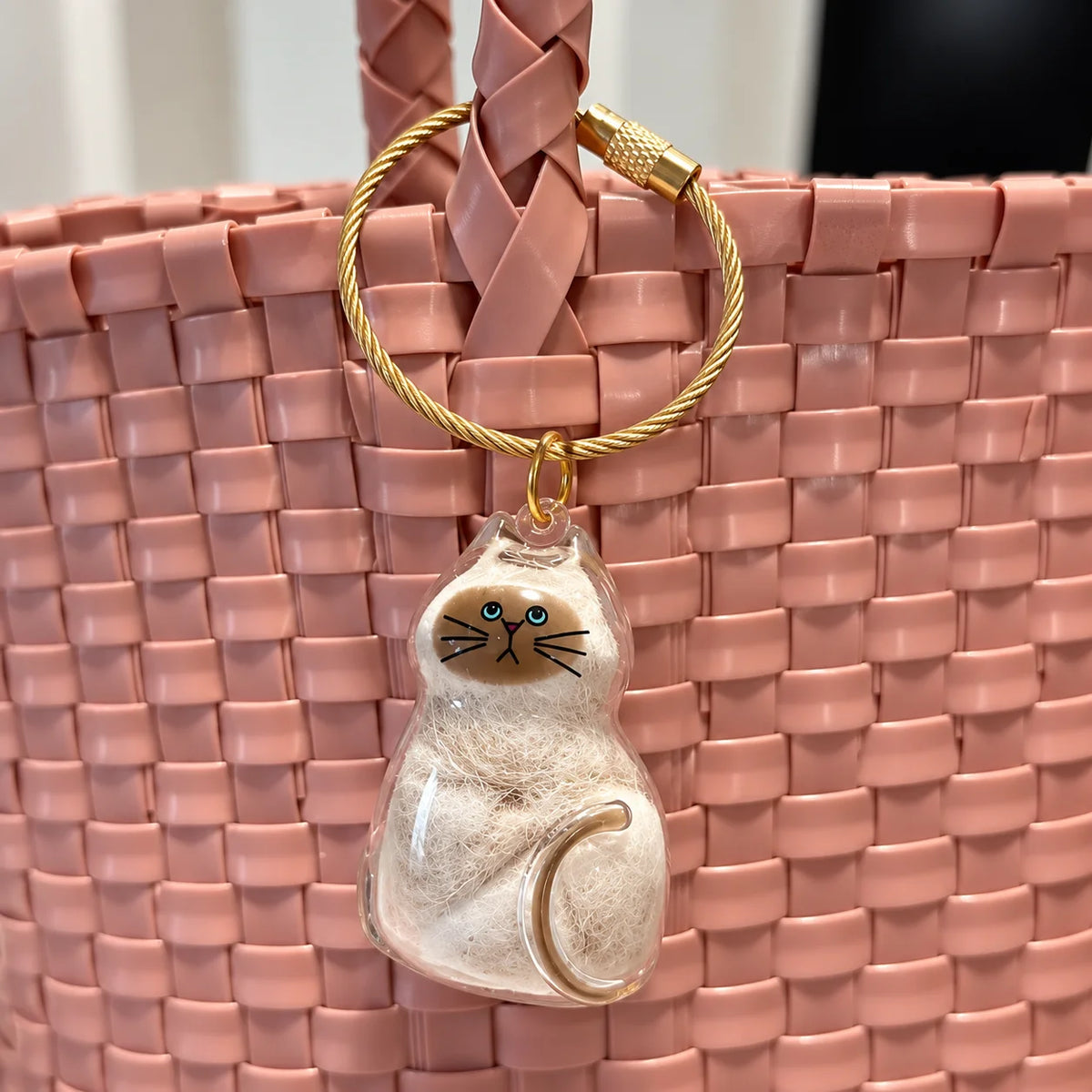 Porte-clés PurrKey en forme de chat accroché à un sac tressé rose pour garder un souvenir félin près de soi